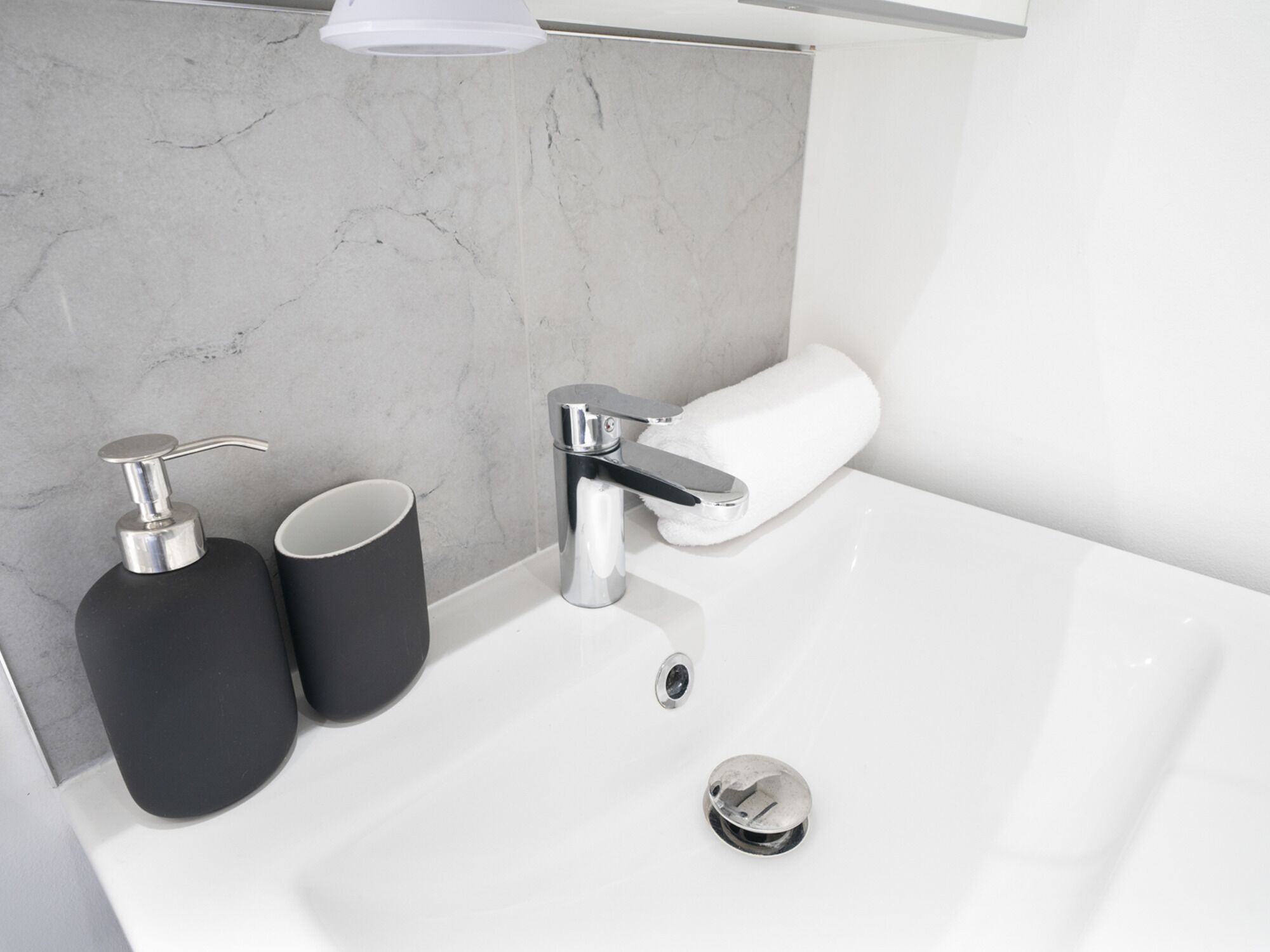 A modern bathroom with a white sink, a chrome faucet, and two black dispensers.