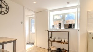 A modern kitchen with a herringbone floor, a wooden table, a metal shelf unit with dishes, and a clock on the wall. - Pass the Keys | The Soak House - Great Hot Tub! (Rye)