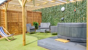An outdoor patio with a wooden pergola, a hot tub, wicker furniture, and a striped lounge chair. - Pass the Keys | The Soak House - Great Hot Tub! (Rye)