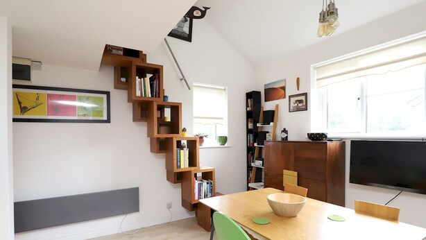 Una sala de estar moderna con una escalera de madera, un televisor de pantalla plana y un comedor con mesa y sillas de madera.