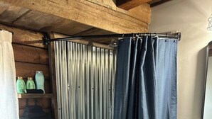 Un espace douche doté d’une porte en métal, d’un rideau de douche bleu, de murs en bois et d’une petite étagère contenant des articles de toilette.