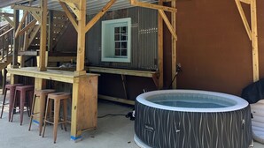 Eine Holzterrasse mit Whirlpool und Barbereich, ein überdachter Außenbereich zum Sitzen und Blick auf das Haus.