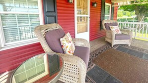 A porch with wicker chairs and a glass table, a red exterior wall, and a white door. - Two Bedroom House Close to Local Favorites (West Lafayette)