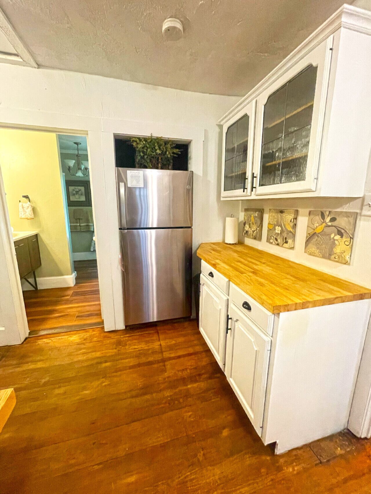 A compact kitchen with white cabinets, a stainless steel refrigerator, and a wooden countertop.