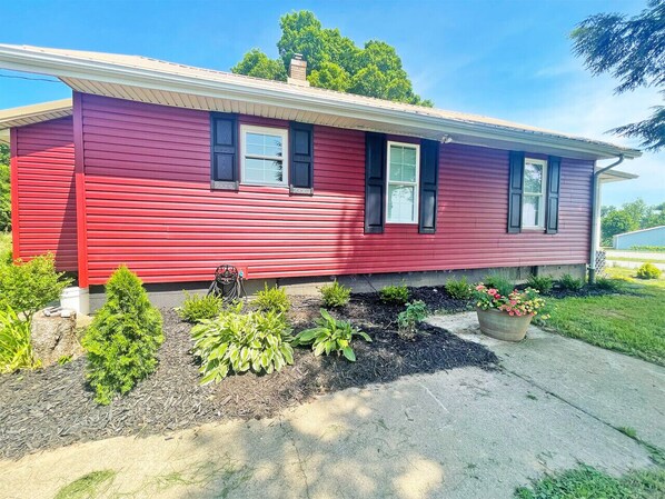 A red house with a front yard, including a garden bed and a small tree.