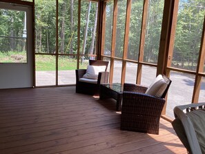 A covered outdoor seating area with wicker furniture and a view of a forested area. - Brand new beautiful, quiet, and spacious 3-bedroom house next to Pickwick Lake (Counce)