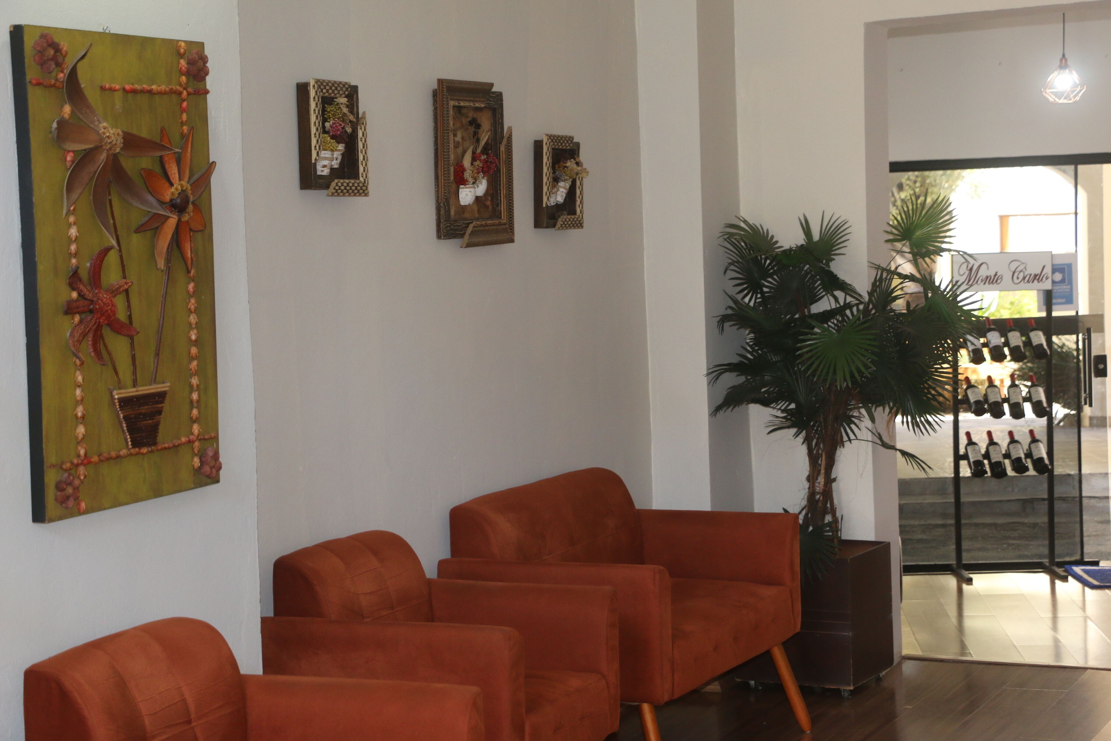 A reception area with a green wall art, three framed pictures, and a row of orange chairs.