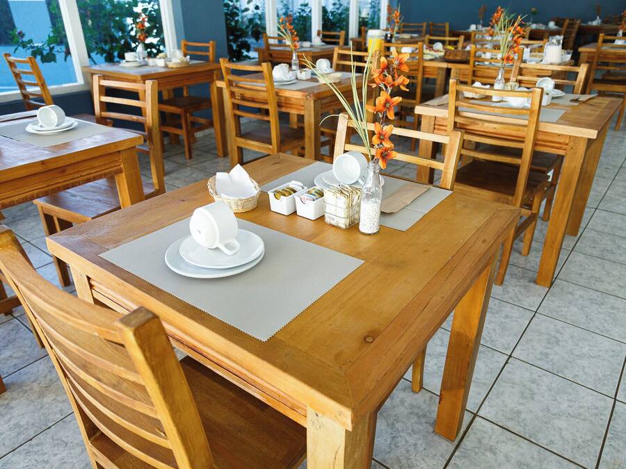 Un restaurant avec des tables et des chaises en bois, disposées dans un espace intérieur vaste et lumineux grâce à de grandes fenêtres.