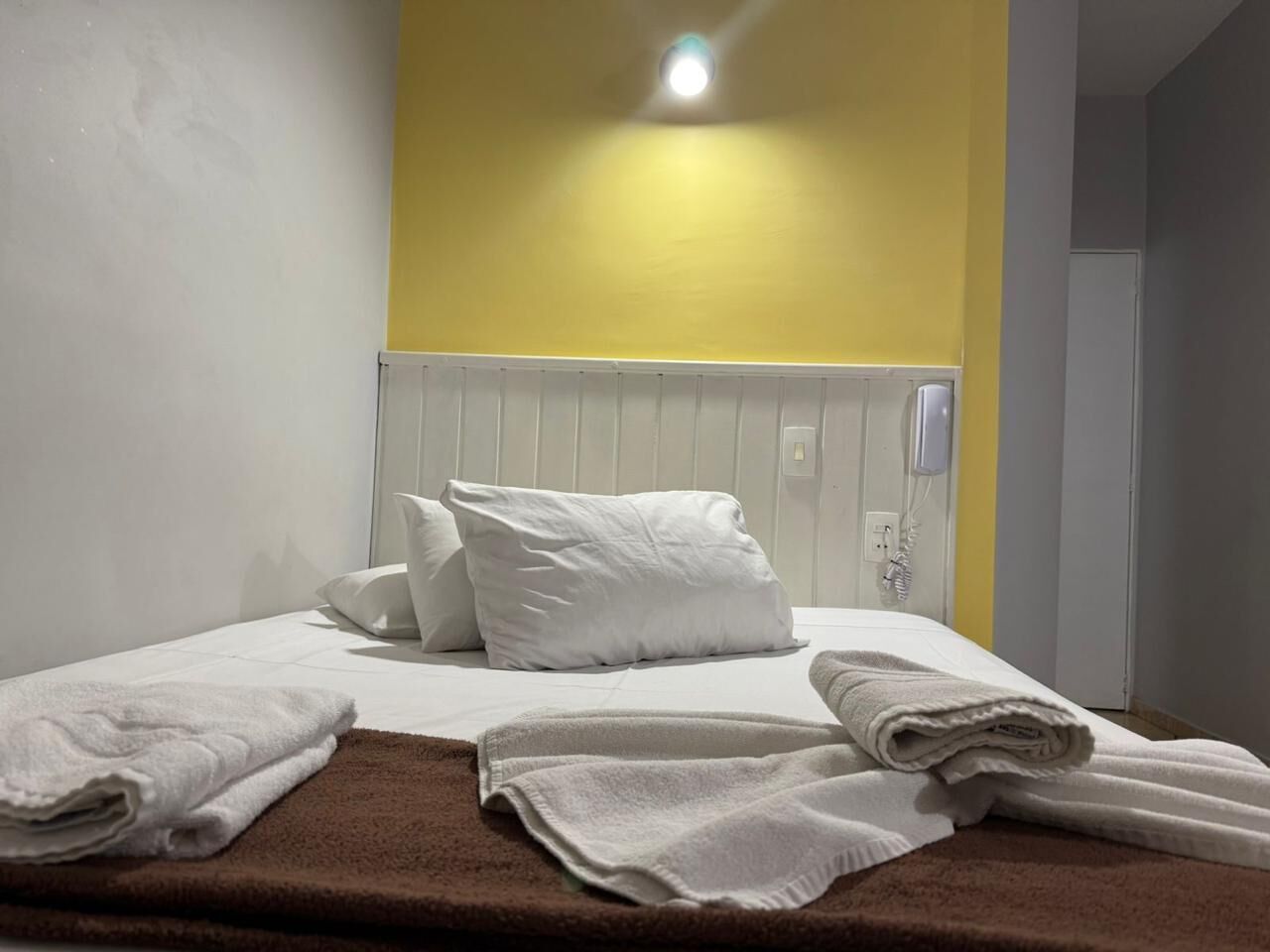 A hotel room with a bed, white pillows, and a brown carpet.