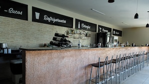 Un espace bar doté d’un long comptoir, de nombreux tabourets et d’étagères remplies de bouteilles et de verres.