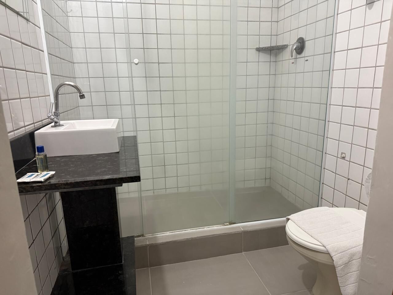 A bathroom with a glass-enclosed shower, a sink with a black countertop, and a toilet.