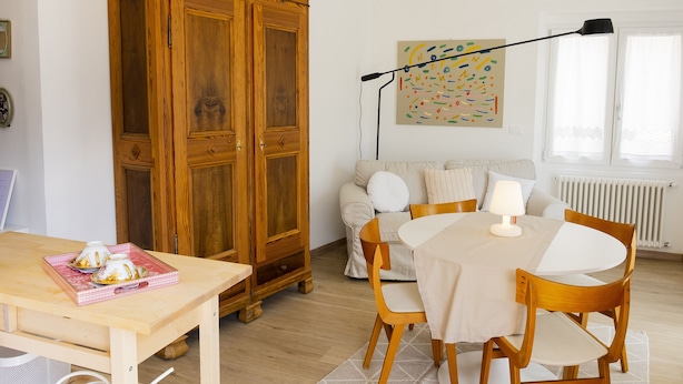 A dining area with a wooden table and chairs, a cabinet, a sofa, and a radiator. - Casa Clelia (Verrès)