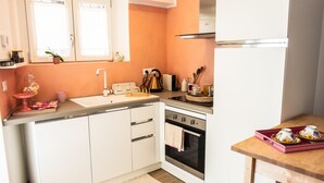 A kitchen with white cabinets, a stainless steel oven, a sink, and a wooden table. - Casa Clelia (Verrès)