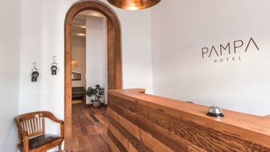 Un espace d’accueil avec un comptoir de réception en bois, un luminaire suspendu et un banc en bois.