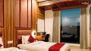 Een hotelkamer met twee bedden, een bureau met lamp, een spiegel en een groot raam met gordijnen.