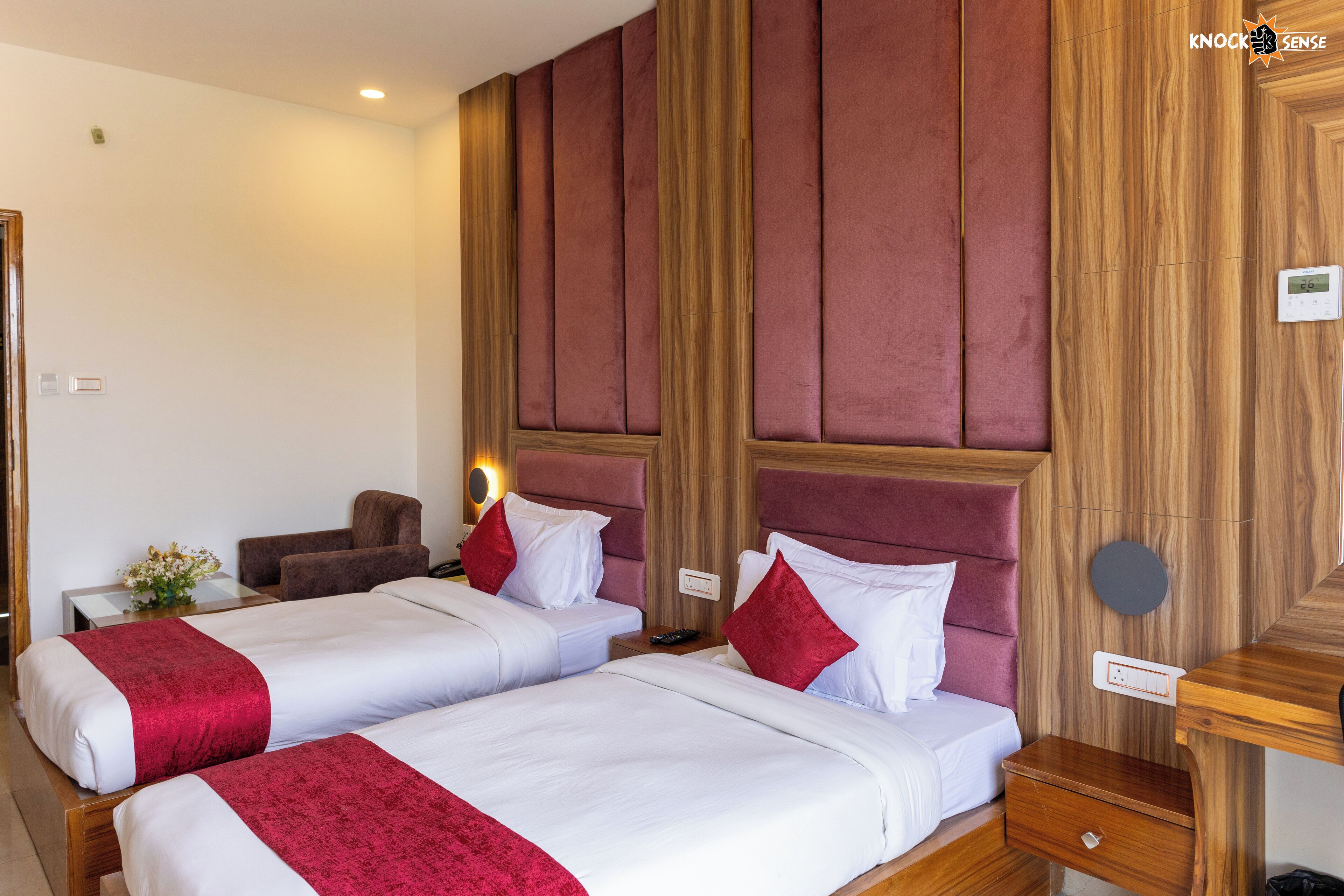 A hotel room with two beds, a wooden headboard, a bedside table, and a small desk.