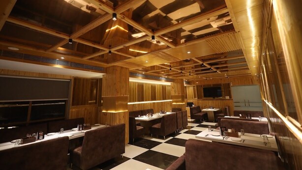 Een restaurant met een schakeerd vloer, houten lambrisering en een hoog plafond met zichtbare balken.