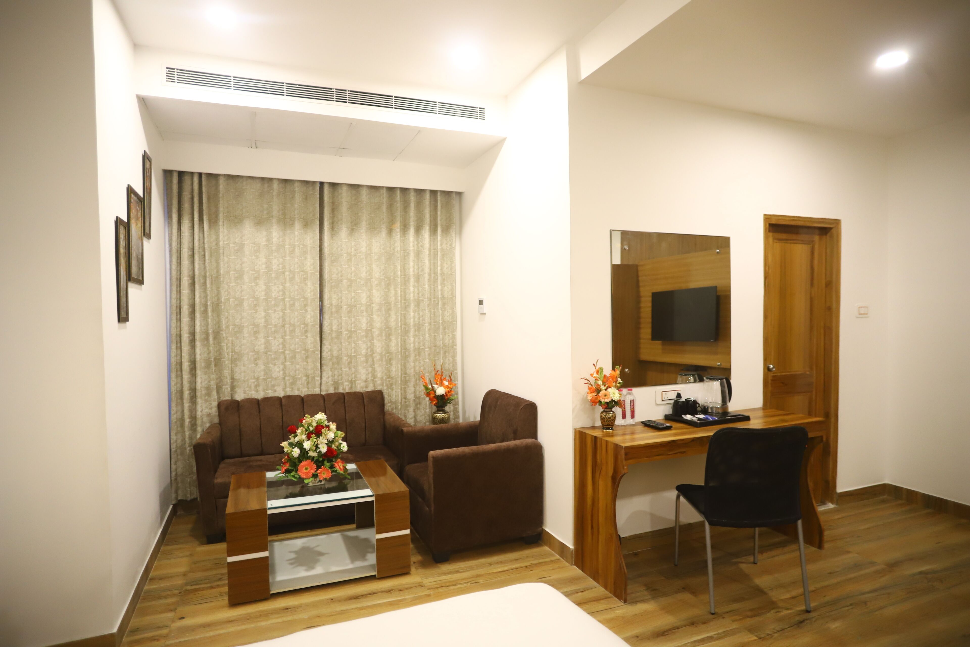 A living room with a sofa, a coffee table with flowers, a TV on a wooden stand, and a wooden desk with a chair.