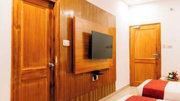 Habitación de hotel con paneles de madera, un televisor de pantalla plana montado en la pared, dos camas con ropa de cama roja y blanca, y puertas de madera.