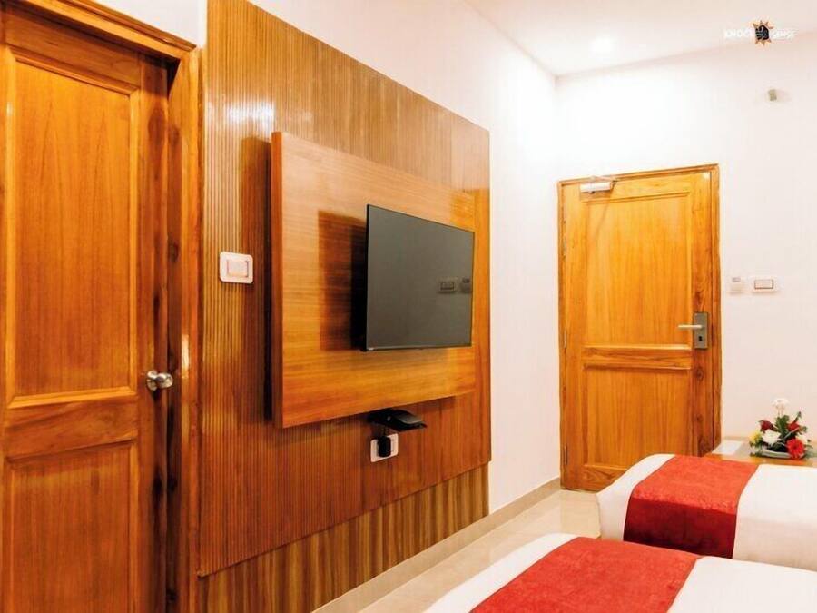 Habitación de hotel con paneles de madera, un televisor de pantalla plana montado en la pared, dos camas con ropa de cama roja y blanca, y puertas de madera.