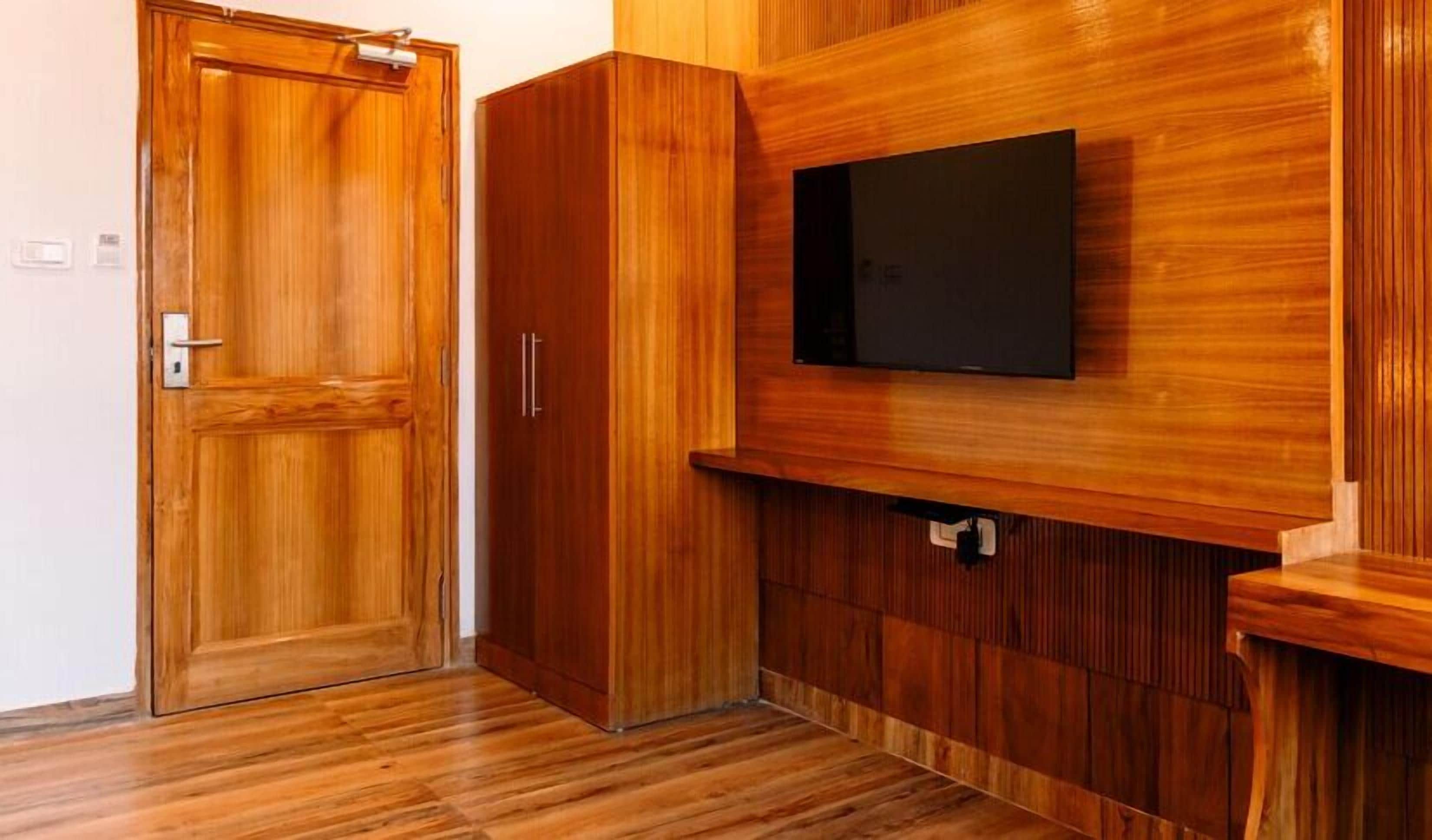 A room with a wooden wardrobe, a television mounted on a wooden panel, and a wooden floor.