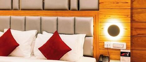 A hotel room with a bed, a bedside table with a phone, and a wall-mounted light.