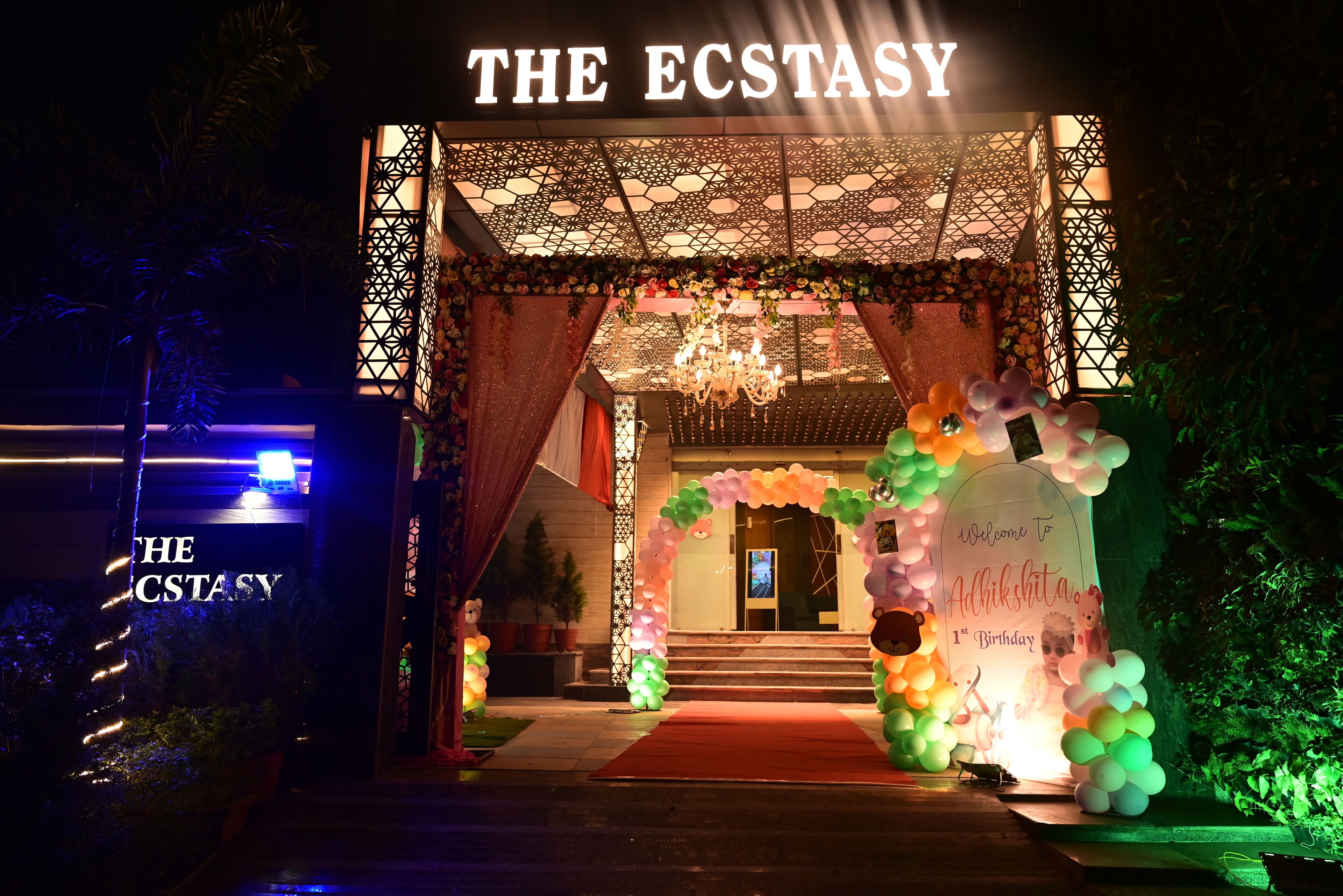 The entrance of The ECSTASY hotel with a red carpet, colorful balloons, and a chandelier.