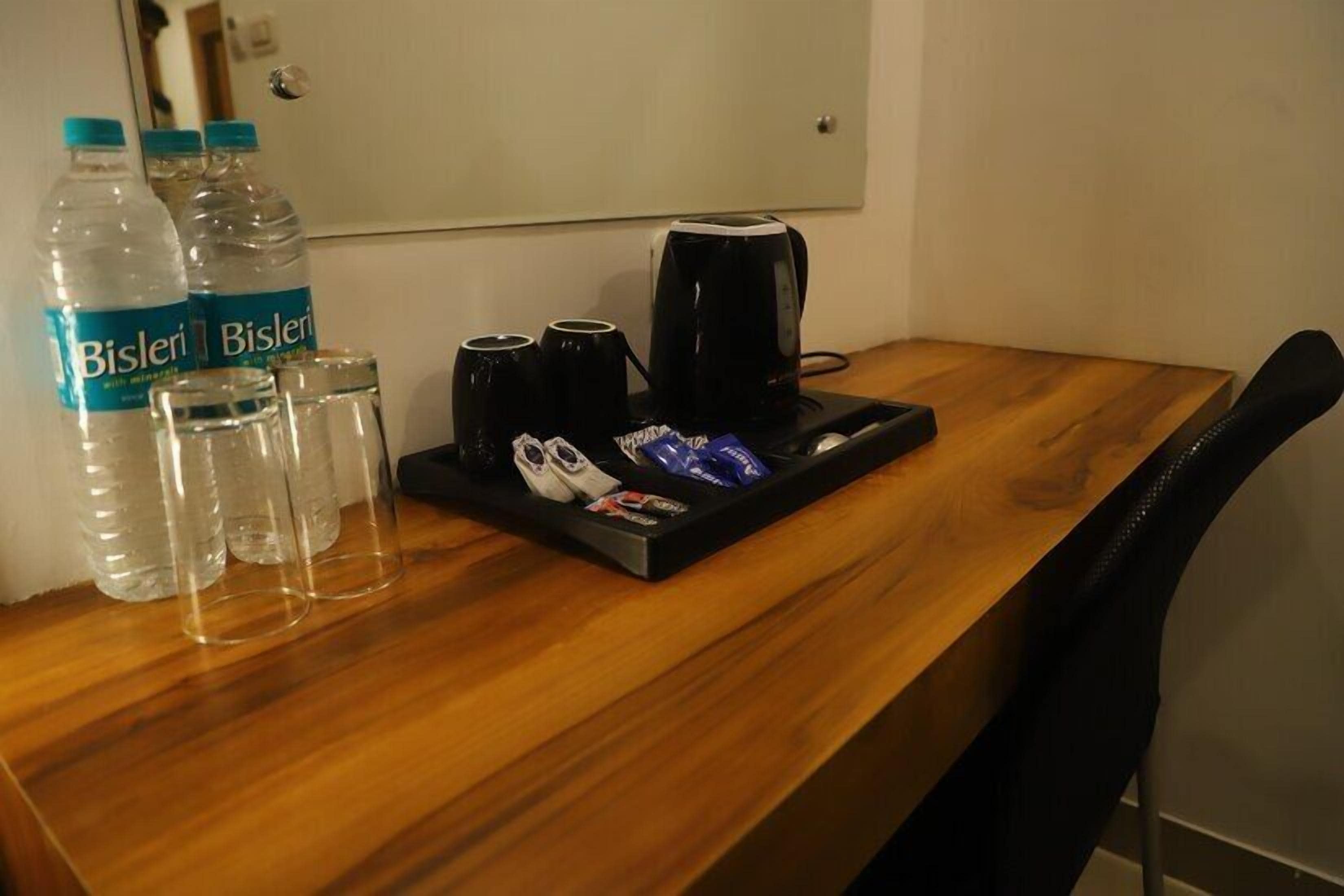 A wooden table with water bottles, glasses, a coffee maker, and a tray with shoes and snacks.