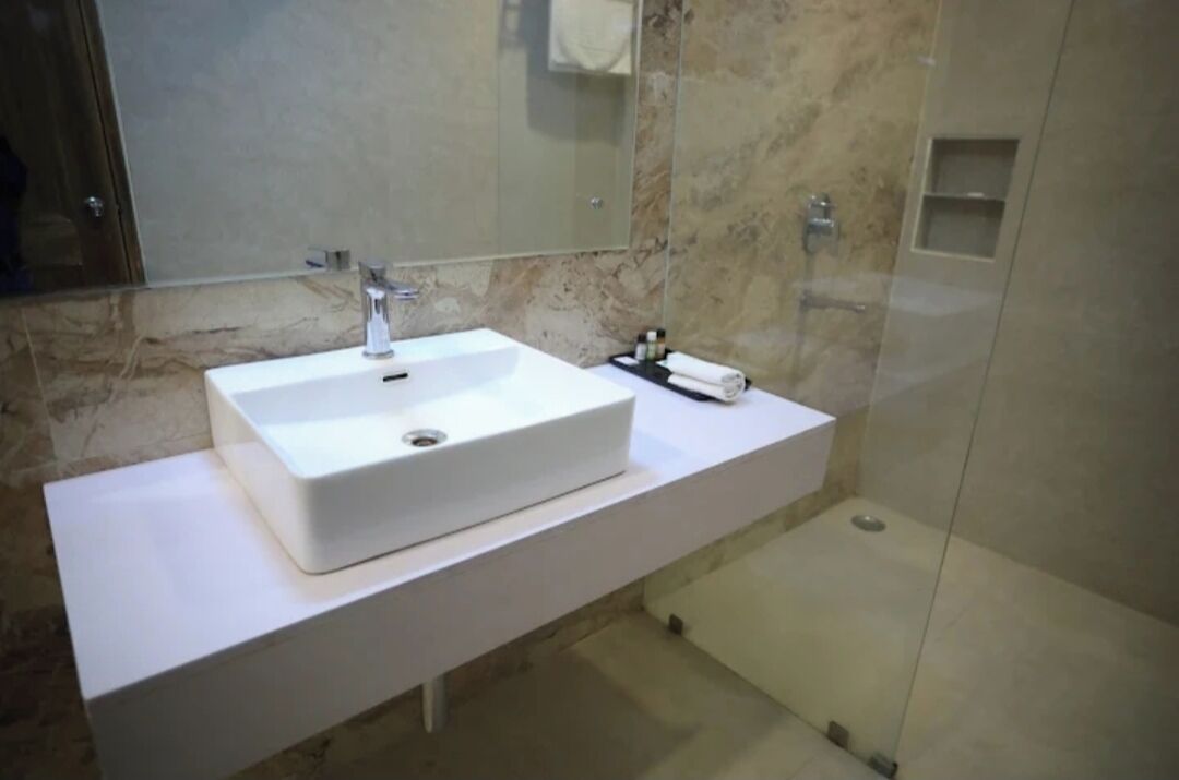 A modern bathroom with a white sink, a mirror, and a shower area.