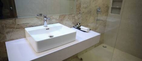 A modern bathroom with a white sink, a mirror, and a shower area.