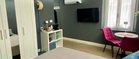 Un dormitorio con cama, armario, escritorio con silla, televisión y ventana con cortinas.