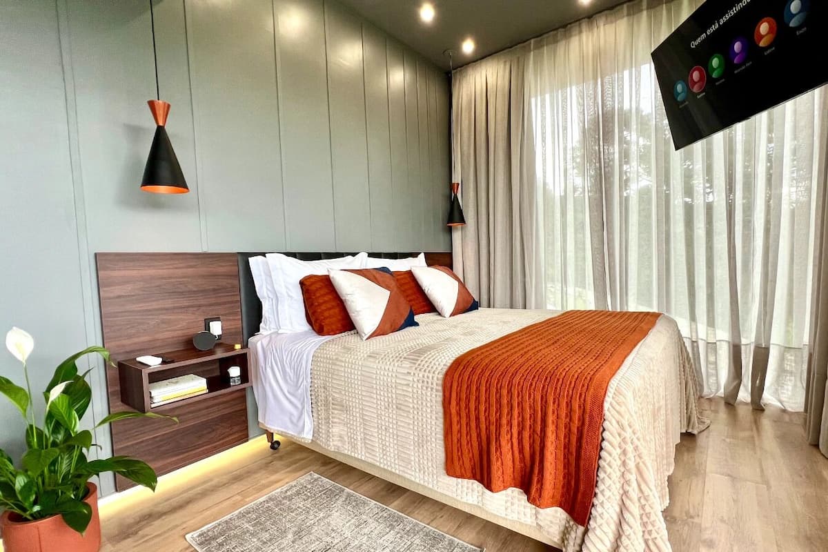 Een moderne slaapkamer met een bed, nachtkastjes, een nachtlampje, een potplant en een groot raam met gordijnen.