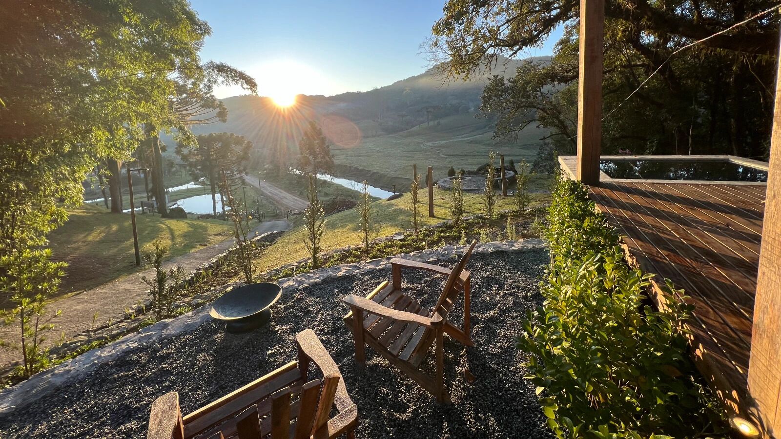 A wooden deck with a fire pit and seating area overlooking a valley with a lake and hills.