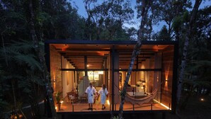 Una cabaña moderna con paredes de vidrio y un interior de madera, rodeada por un bosque.