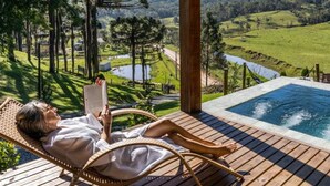 Una persona relajándose en una silla de mimbre junto a una piscina con vistas a un paisaje verde y una masa de agua.
