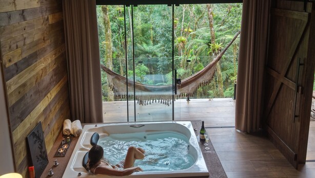 Una habitación de madera con un ventanal grande, una bañera y una hamaca.