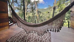 Una hamaca en una terraza de madera con vista a un bosque y montañas.