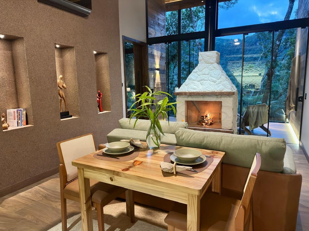 A modern interior with a dining table, chairs, a sofa, a fireplace, and a view of the outdoors.