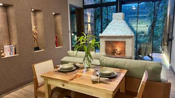 A modern interior with a dining table, chairs, a sofa, a fireplace, and a view of the outdoors.