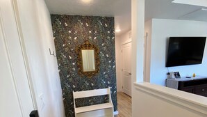 Ein Flur mit strukturierter Tapete, einer weißen Bank, einem Teppich und einem an der Wand befestigten Fernseher.