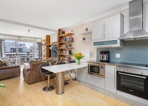 A modern kitchen with stainless steel appliances, a dining area with a glass table, and a cozy seating area with a sofa. - The Tygervalley Escape (Cape Town)