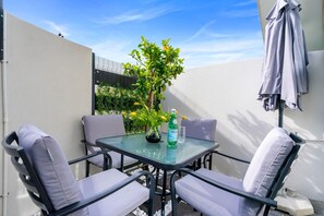 A small outdoor patio with a glass table and four cushioned chairs, a potted plant, and a bottle of water.