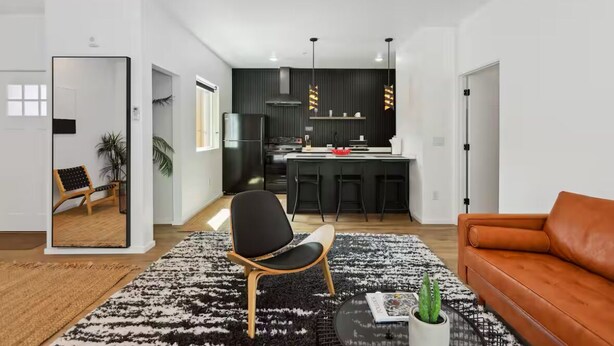 Un salón moderno con alfombra blanco y negro, una silla de madera, un sofá de cuero marrón y una mesita con una planta.