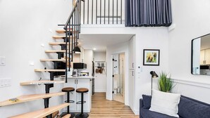 A modern apartment with a staircase leading to a loft, a living area with a sofa and a coffee table, and a kitchen area with bar stools. - Covelet Hideaway (Blaine)