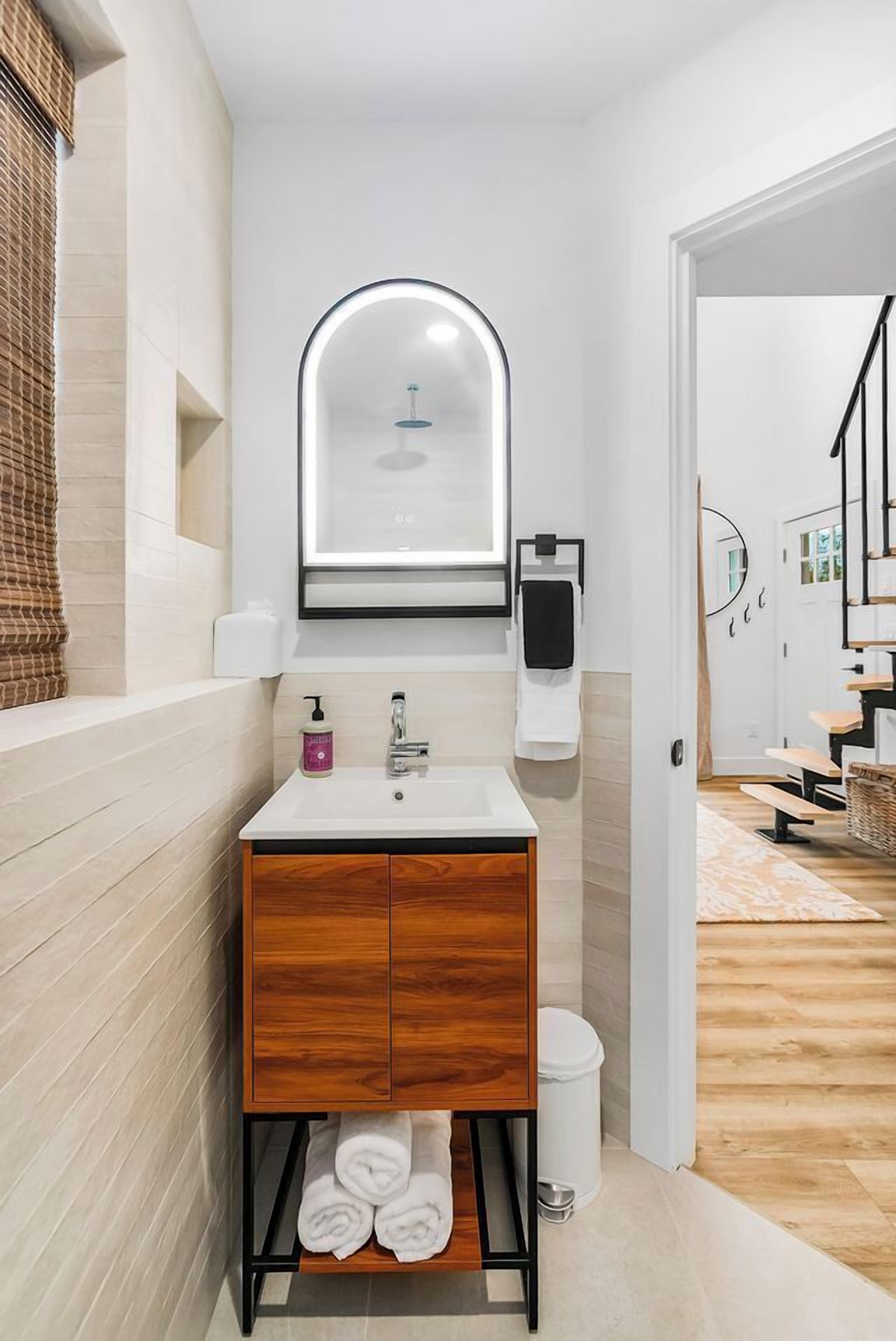 Un baño moderno con un tocador blanco, un espejo con luz, un dispensador de toallas y un armario de madera.