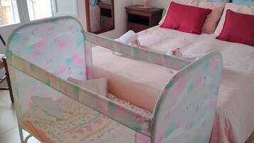 Ein Schlafzimmer mit einem Babybett, einem Bett mit rosa Bettwäsche, einem Nachttisch und einem Spiegel.
