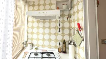 A kitchen with a gas stove, a window with blinds, and patterned wall tiles.