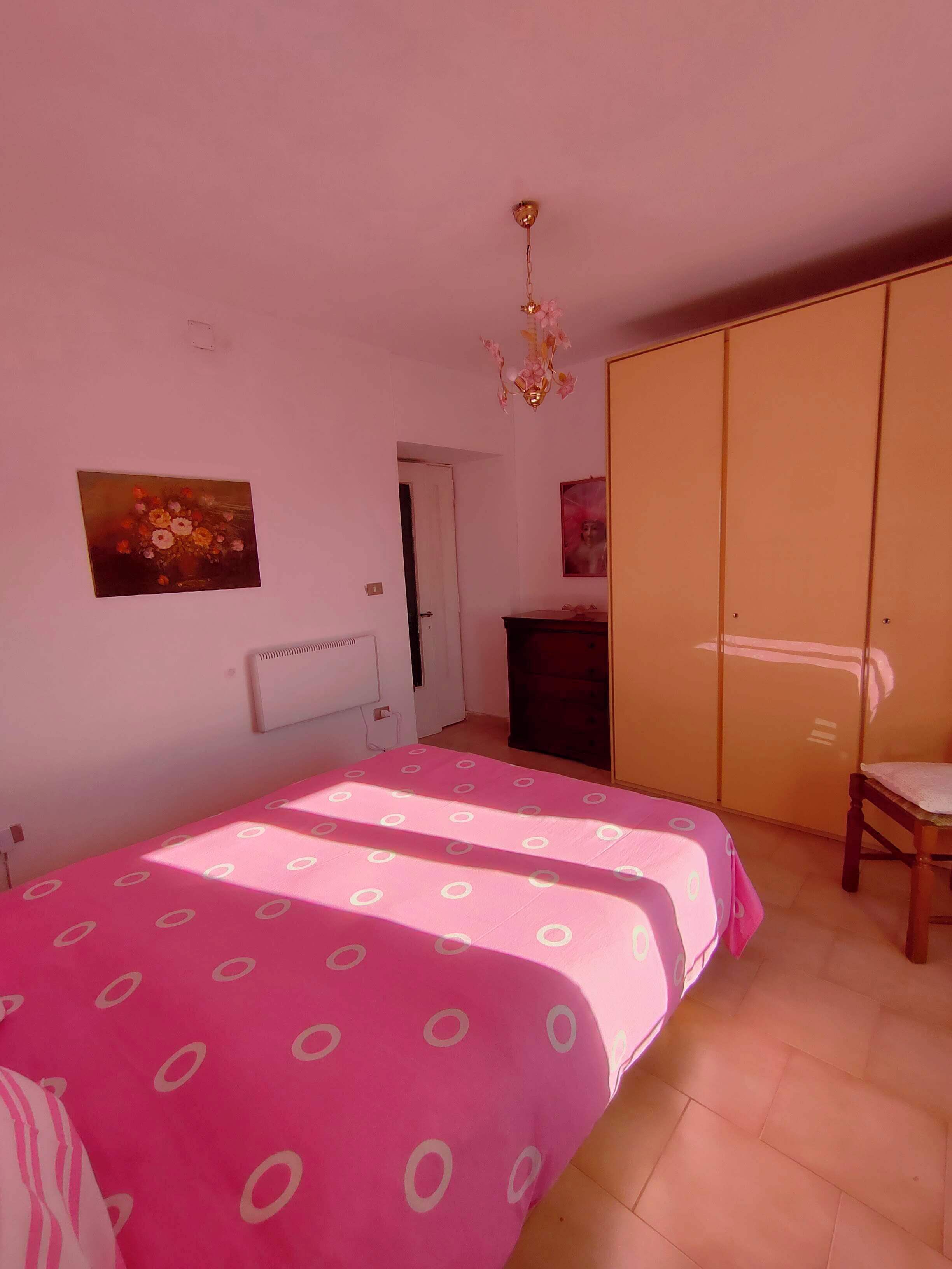 A bedroom with a bed, a wardrobe, a radiator, and a painting on the wall.