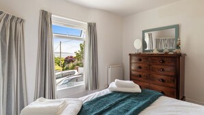 A bedroom with a bed, a dresser, a window with curtains, and a view of the outside. - Melbourne - Sea Views and Parking (Saundersfoot)