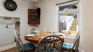 A dining area with a wooden table set for four, white chairs, and a clock on the wall. - Melbourne - Sea Views and Parking (Saundersfoot)